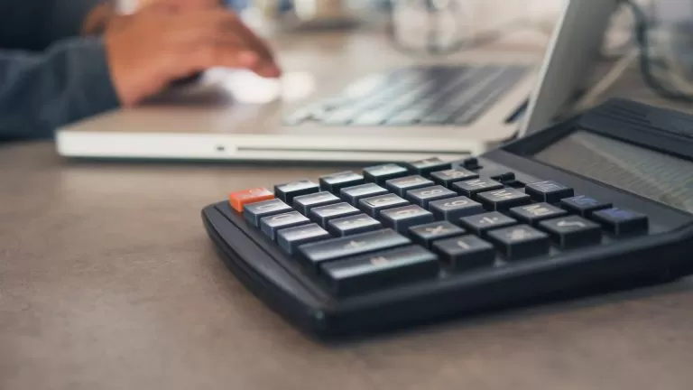 The Calculator Is Placed On An Office Table With A Laptop And Th